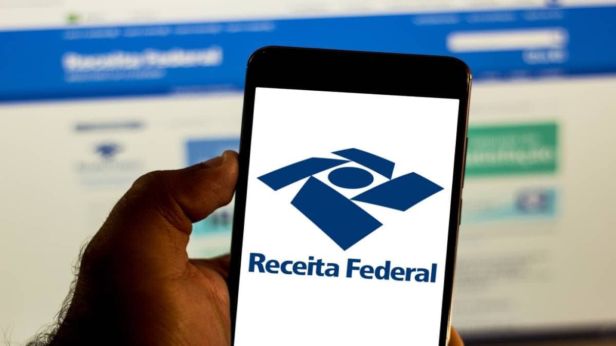 Tela de navegador no site da Receita Federal de fundo e celular em primeiro plano com logo