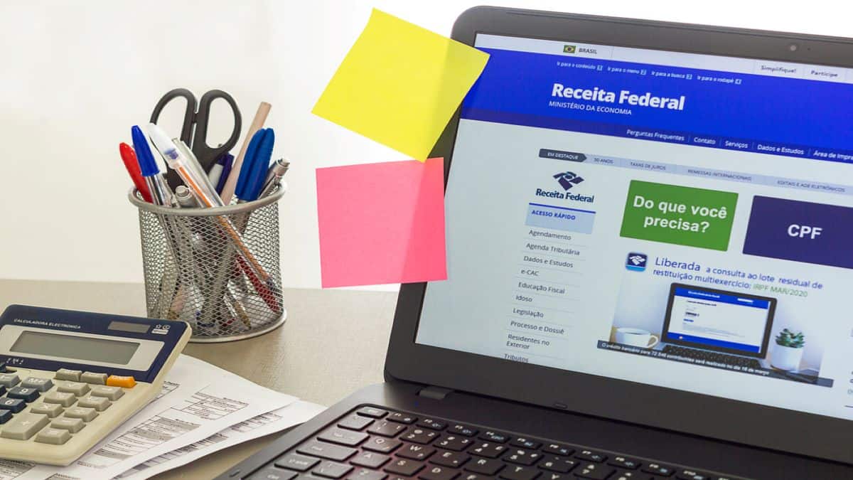 notebook com tela em aberto no site da Receita Federal e papéis de lembretes colados na parte lateral da tela